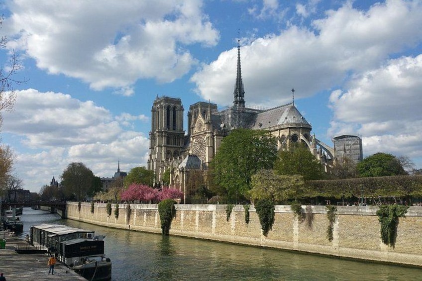Notre-Dame Cathedral, a historic cathedral with a tall spire, along a river with a stone wall and trees. 5
