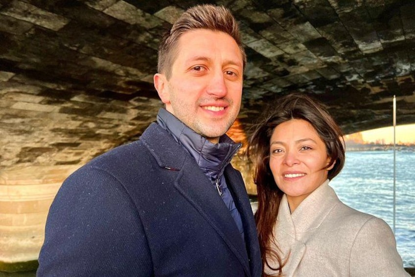 A man and a woman standing under a bridge with a body of water in the background. 4