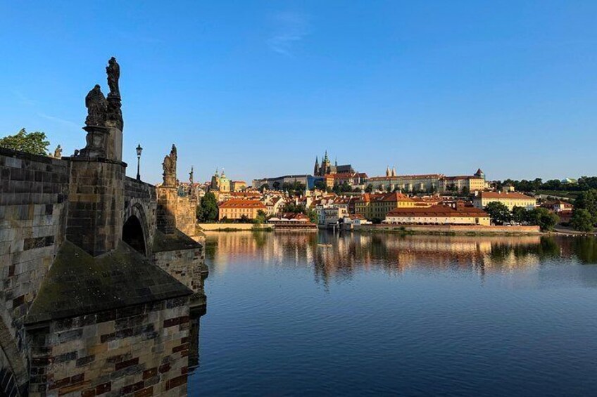 A historic stone bridge with statues, a calm river, and a cityscape with buildings and a church in the background. 5