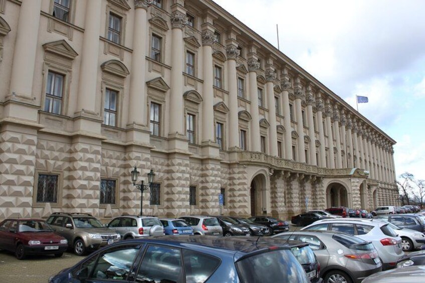 A large, classical building with columns and arched windows, surrounded by a parking lot with various cars. 5