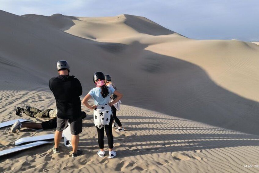 Three people standing on a sand dune with a desert landscape in the background. 1