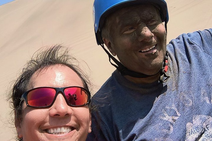 Two people wearing helmets, one in a blue shirt and the other in a dark shirt, with a sandy landscape in the background. 3