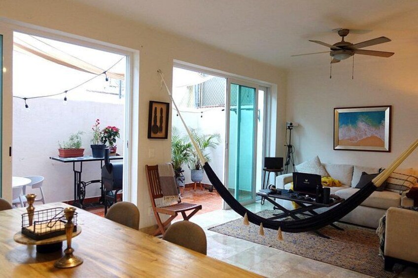 A living room with a hammock, a dining table, chairs, a laptop, and a painting on the wall. 3