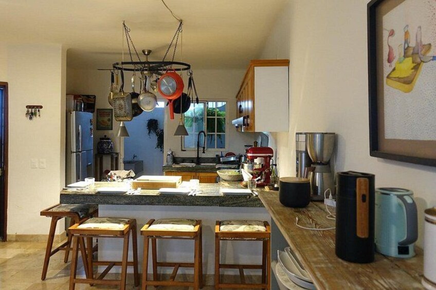 A kitchen with a central island, bar stools, hanging pots, a coffee maker, and a refrigerator. 5