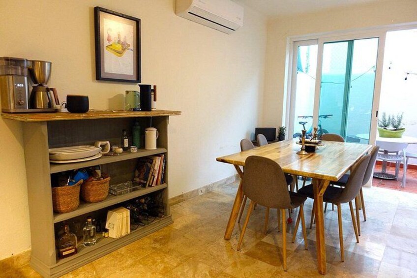 A dining area with a wooden table and chairs, a kitchen counter with shelves, and a sliding glass door leading to an outdoor space. 2