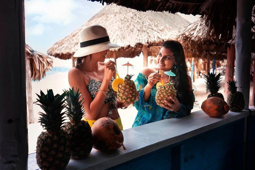 Two people at a beachside bar with tropical drinks and pineapples. 1