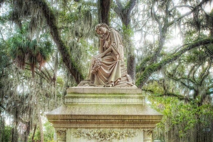 A stone statue of a woman seated on a pedestal surrounded by trees. 3