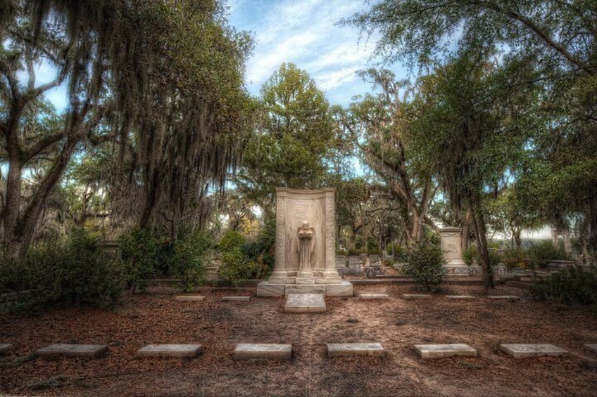 A cemetery with tombstones, a central monument, and trees with Spanish moss. 2