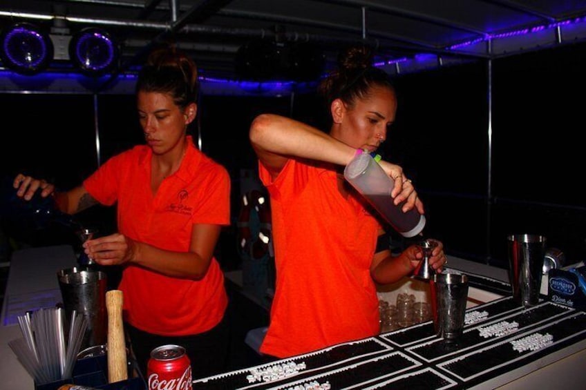 Dos personas con camisas rojas preparando bebidas en un bar, con varias botellas y una lata de Coca-Cola a la vista. 4