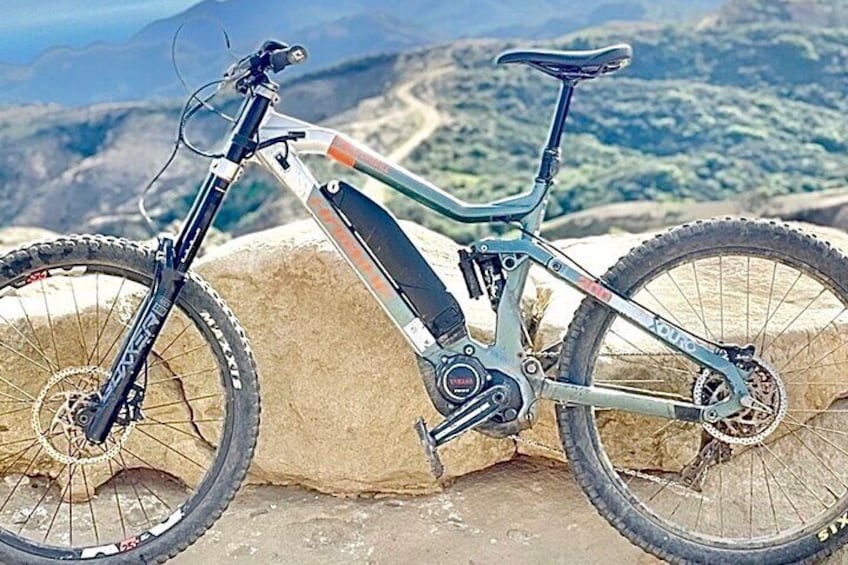 A mountain bike leaning against a rock with a mountainous landscape in the background. 2