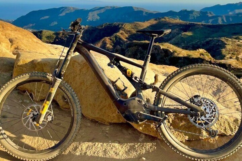 A mountain bike on a rocky outcrop with a scenic view of mountains in the background. 4