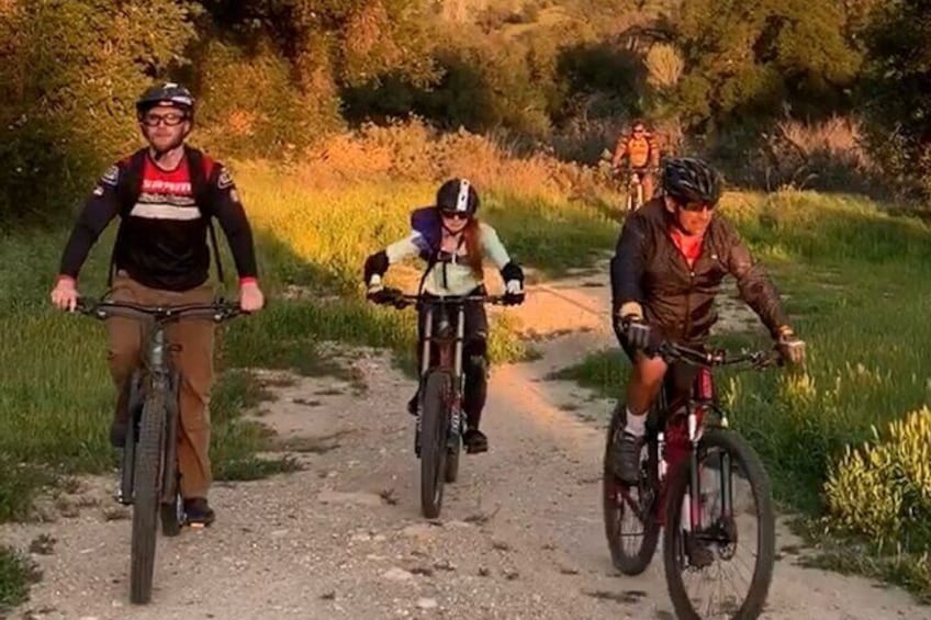 Three cyclists on a dirt path surrounded by greenery. 5