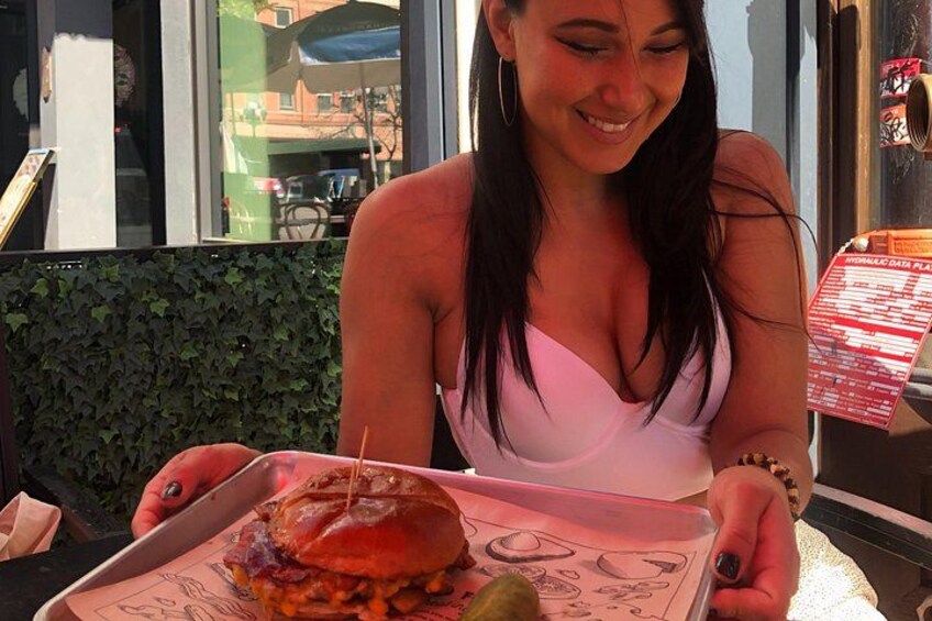 A person holding a tray with a burger and a pickle. 4