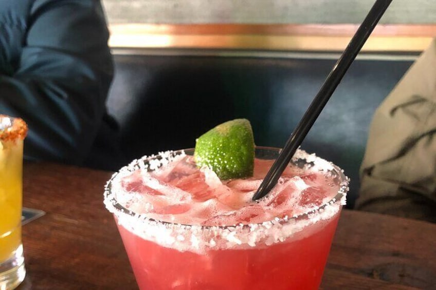 A cocktail with a lime garnish and a salted rim, served in a glass with a black straw. 3