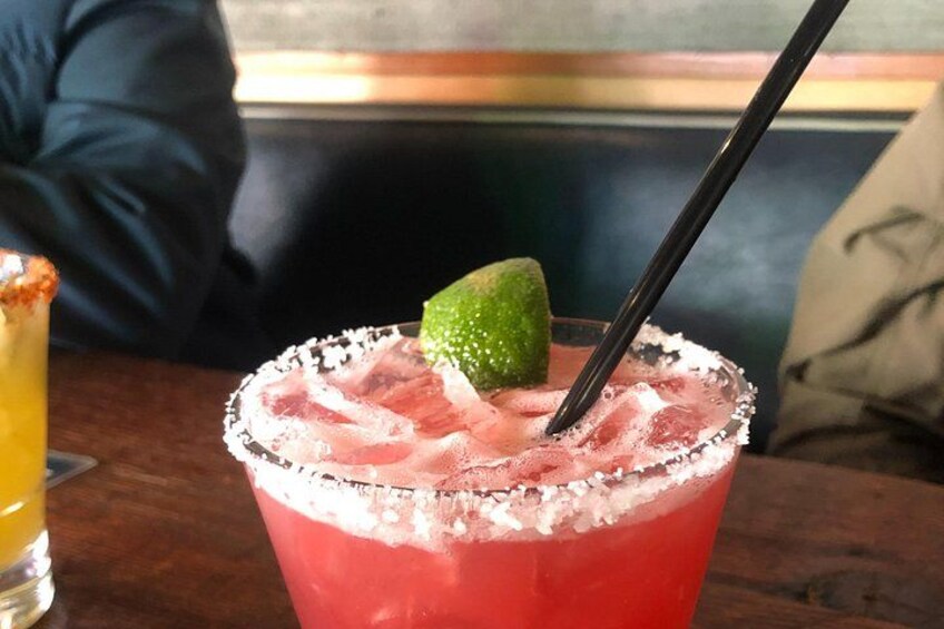 A red cocktail with a lime garnish and a salted rim, a black straw, and a glass of yellow drink in the background. 2