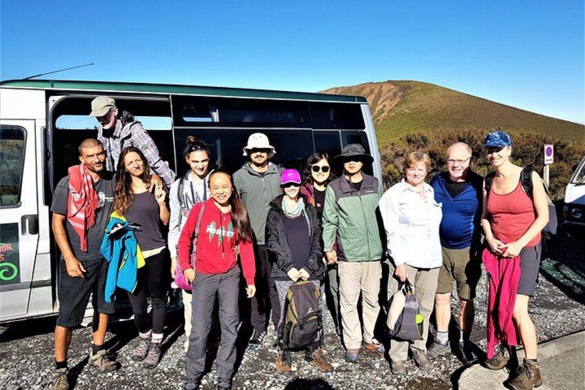 A group of people standing in front of a white van with a mountainous landscape in the background. 4