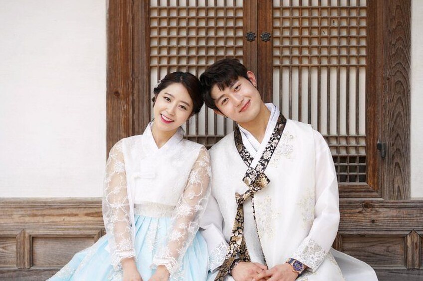 A couple dressed in traditional attire sitting in front of a wooden gate. 4