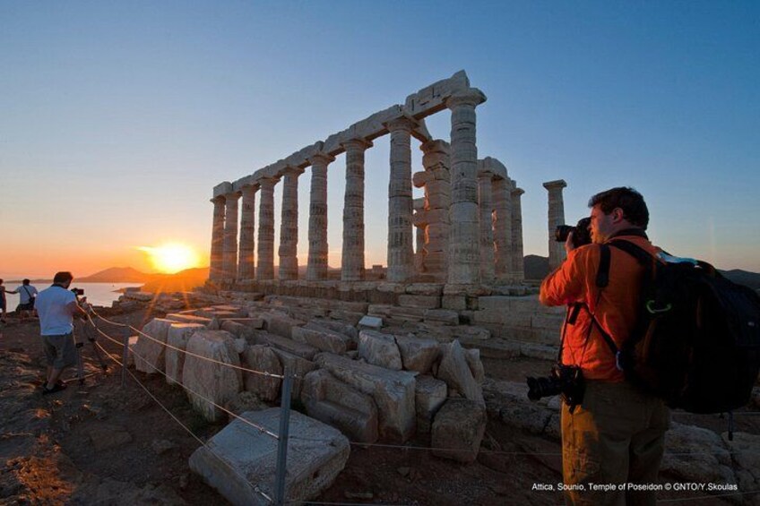 Ancient ruins with columns, a sunset in the background, and people taking photos. 5
