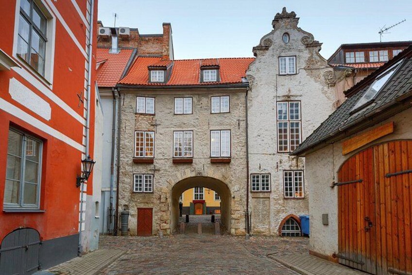A cobblestone street with historic buildings, a stone archway, and a wooden door. 2