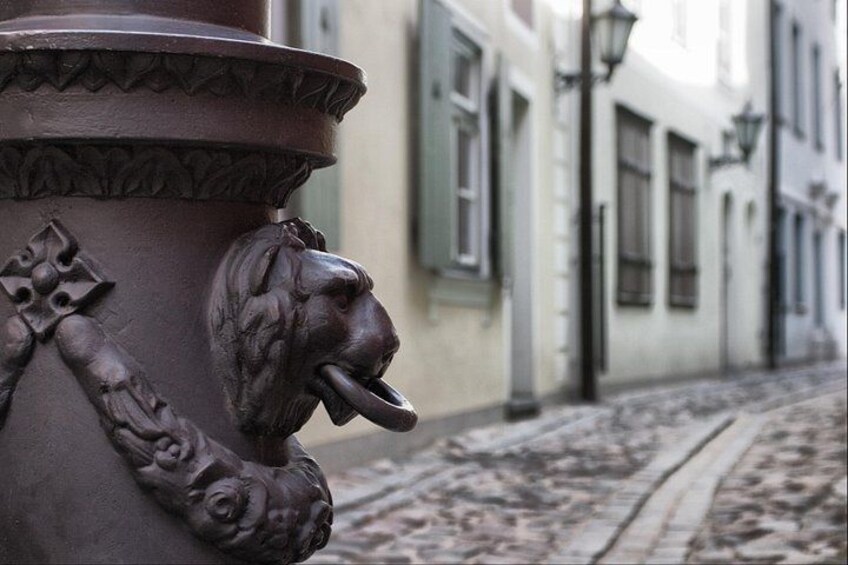 A street lamp, a lion head sculpture, and a cobblestone street. 3