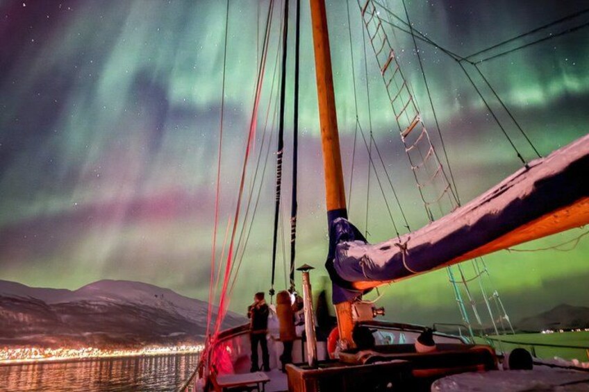 A sailboat with a person standing at the bow, a person on the deck, and a mountainous landscape in the background. 5