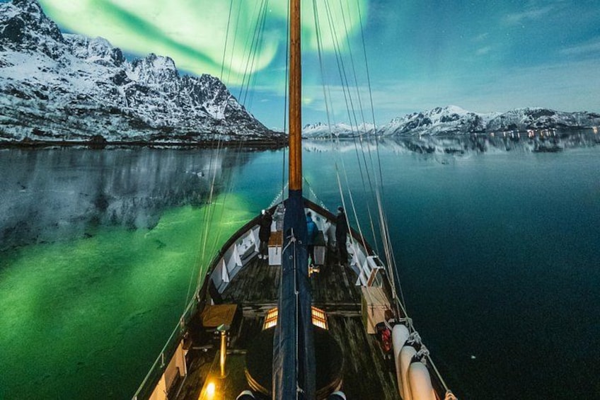 En båd på en stille sø med snedækkede bjerge i baggrunden og nordlys på himlen. 1