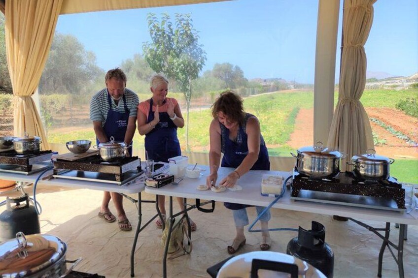 Three people cooking outdoors with cooking equipment and a view of a field in the background. 2