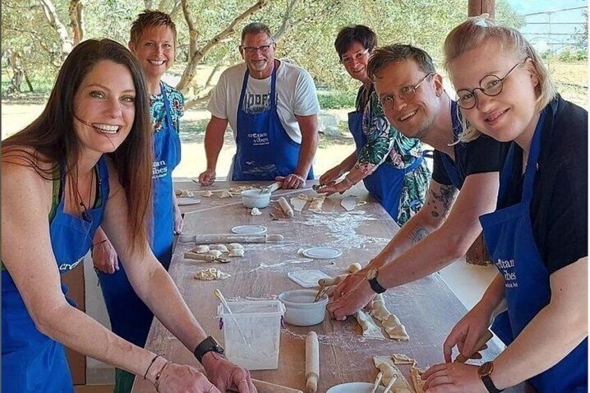 A group of people wearing aprons, working together at a table with dough and baking tools. 1