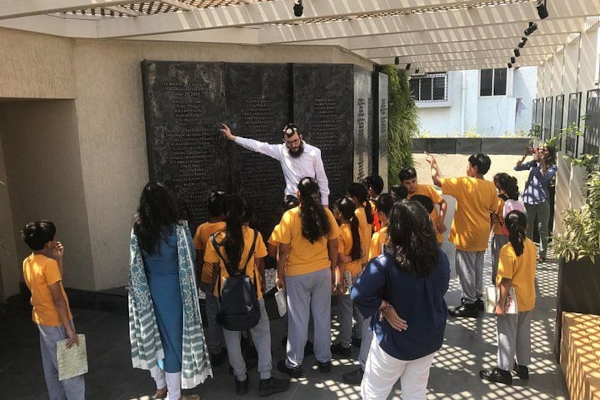 A group of people gathered around a large black plaque outdoors, with a person pointing at it. 1