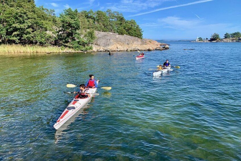 Three kayaks on a calm river with people paddling, surrounded by greenery and rocks. 1