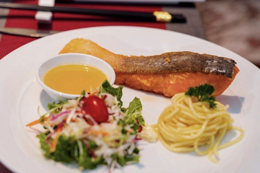 A plate with a piece of salmon, a small bowl of sauce, a salad, and spaghetti. 3