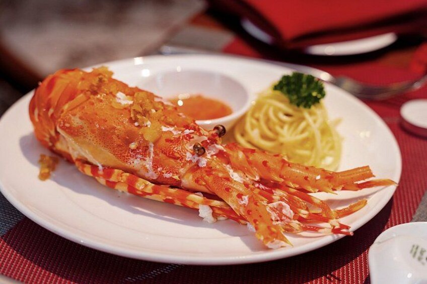 A lobster tail on a plate with pasta and a small bowl of sauce. 2