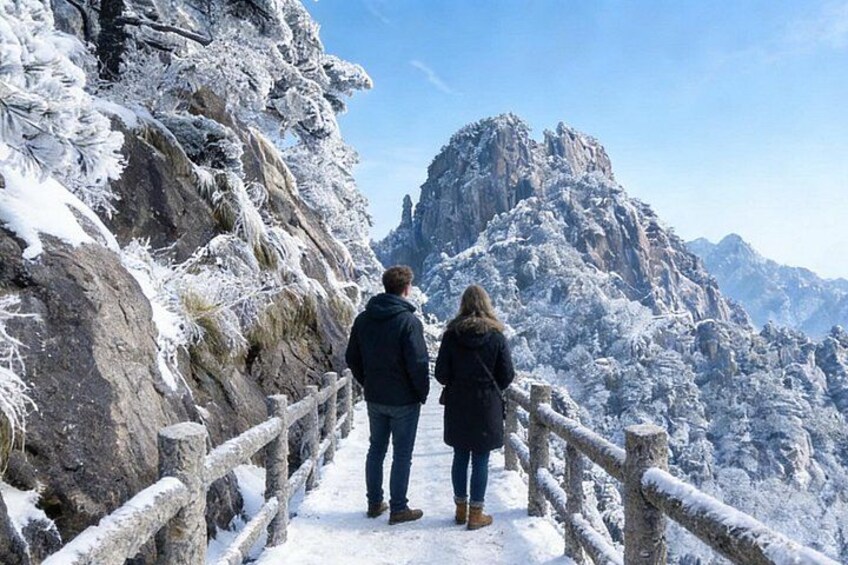 A snowy mountain path with wooden railings, a rocky cliff, and a person standing at the end of the path. 1