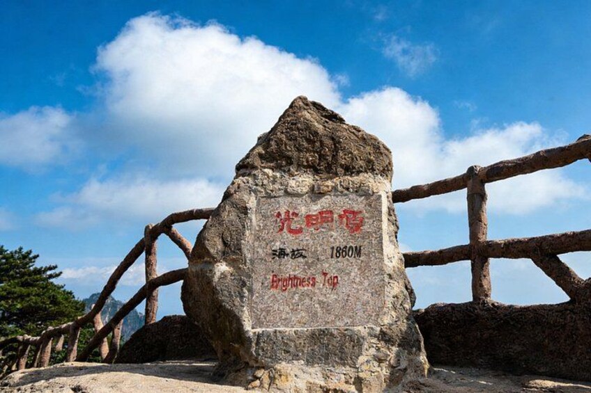A stone monument with inscriptions, a wooden fence, and a clear blue sky with clouds. 4