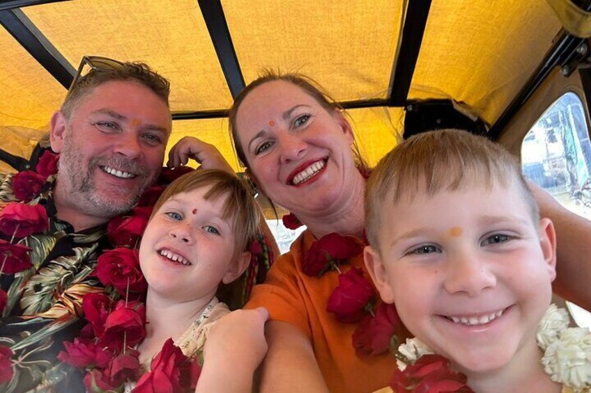 Una familia de cuatro personas en un vehículo con toldo amarillo, usando guirnaldas de flores. 1