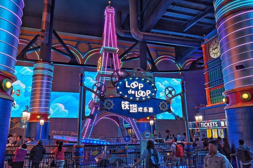 A brightly lit amusement park with a large illuminated Eiffel Tower, ticket booths, and various rides. 3