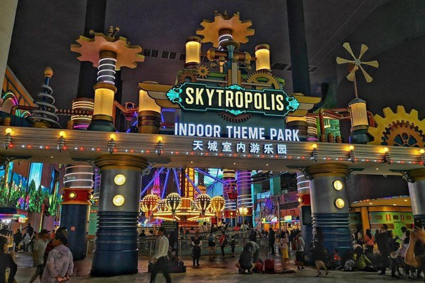 Een overdekt themapark met een bord waarop staat 'SKYTROPOLIS INDOOR THEME PARK' en diverse mechanische constructies. 3