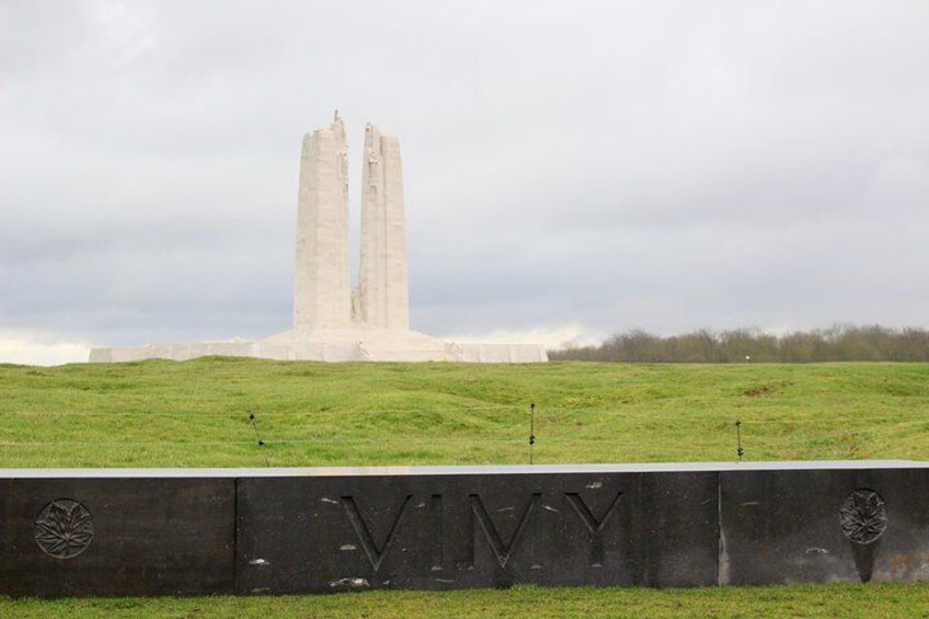 A large concrete monument with two tall pillars, a grassy field, and a wall with the letters 'VIVY' engraved. 3