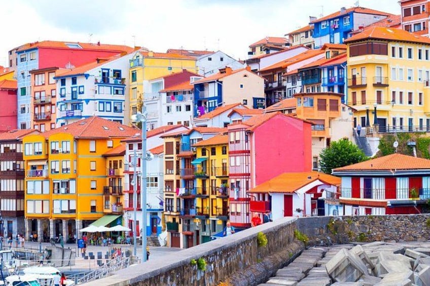 A colorful coastal town with multi-story buildings, a stone wall, and a marina with boats. 4