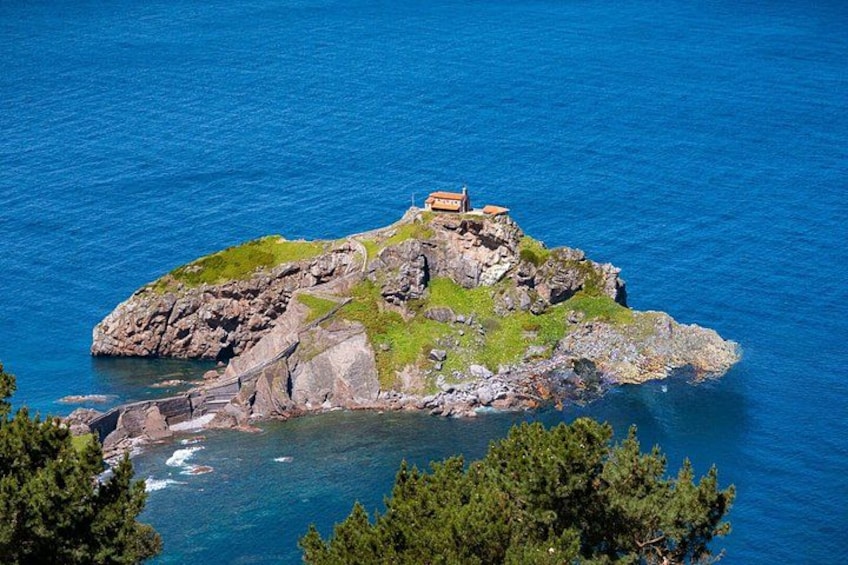 A rocky island with a small building, surrounded by clear blue water and green vegetation. 3