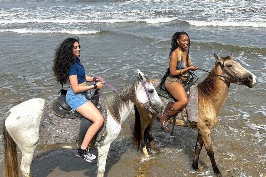 Two people riding horses on a beach with waves in the background. 4