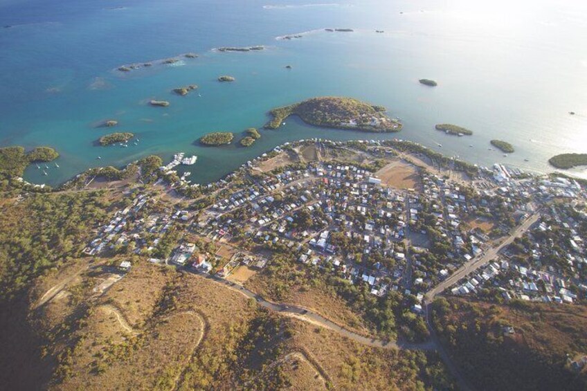An aerial view of a coastal town with a dense cluster of buildings, surrounded by a network of roads and small islands in the water. 2