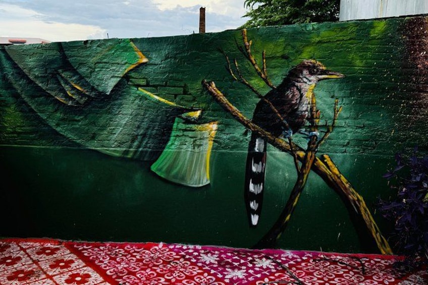 A mural of a bird on a branch, a red patterned cloth, and a green wall. 4