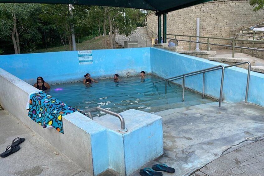 A swimming pool with people in it, a covered area, and a brick wall in the background. 4