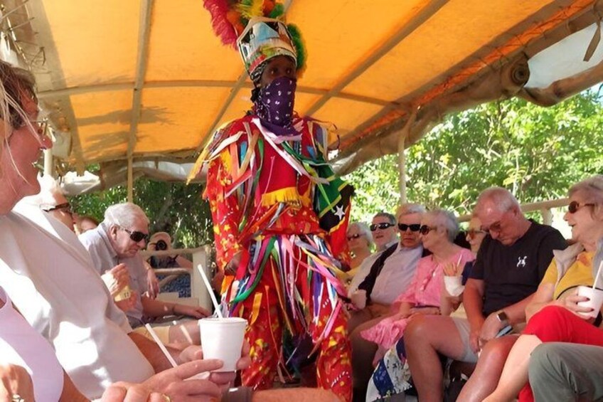 A person in a colorful costume with a feathered headdress, seated under a yellow canopy, surrounded by people. 3