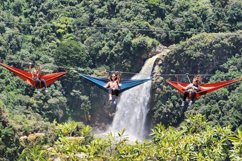 People suspended in hammocks over a waterfall in a forested area. 1