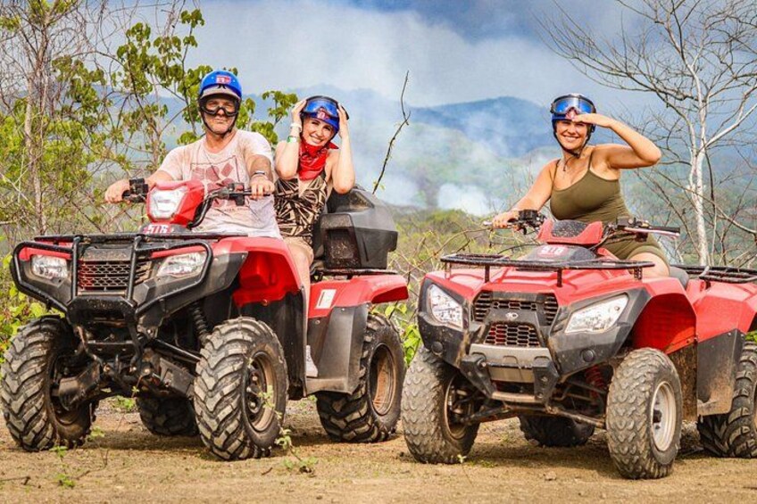 Two people on ATVs in a natural setting with trees and mountains in the background. 3
