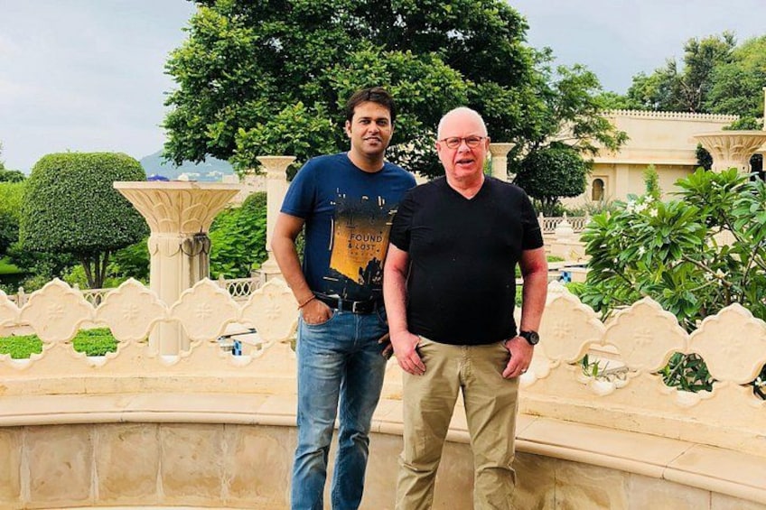 Two people standing in front of a fountain with ornate designs and a well-maintained garden in the background. 5
