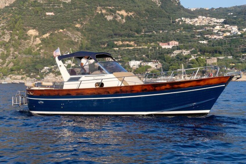 Un barco azul con cabina navegando en aguas tranquilas, con una costa montañosa al fondo. 4