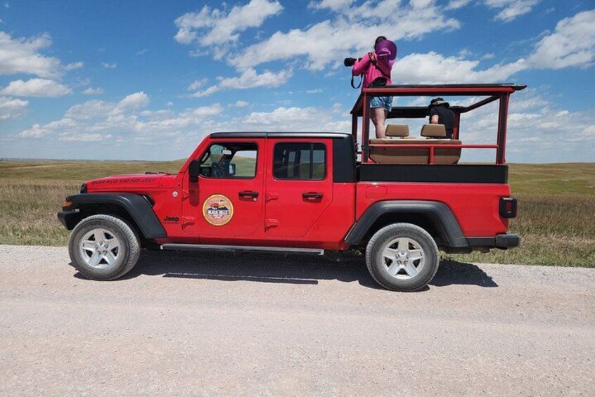Un Jeep rosso con portapacchi, una persona che scatta una foto e un prato erboso sullo sfondo. 2